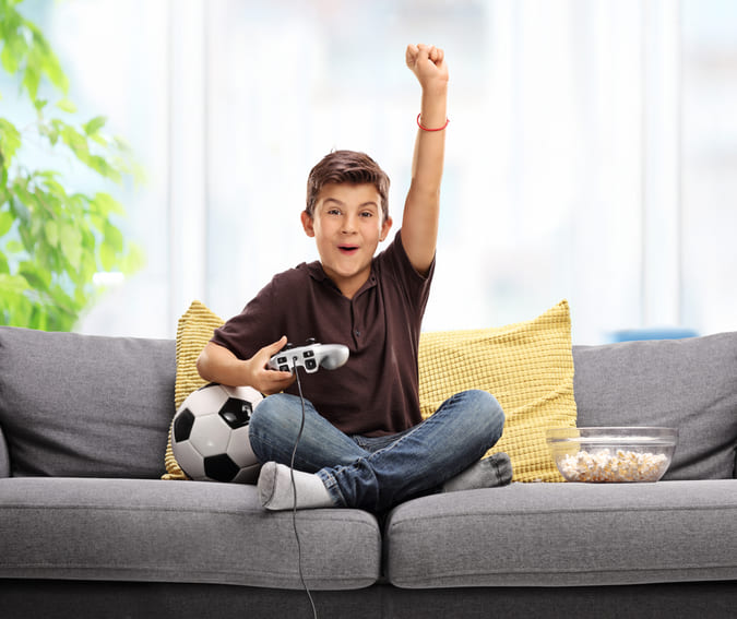 boy feeling happy playing game console with soccer ball beside him.