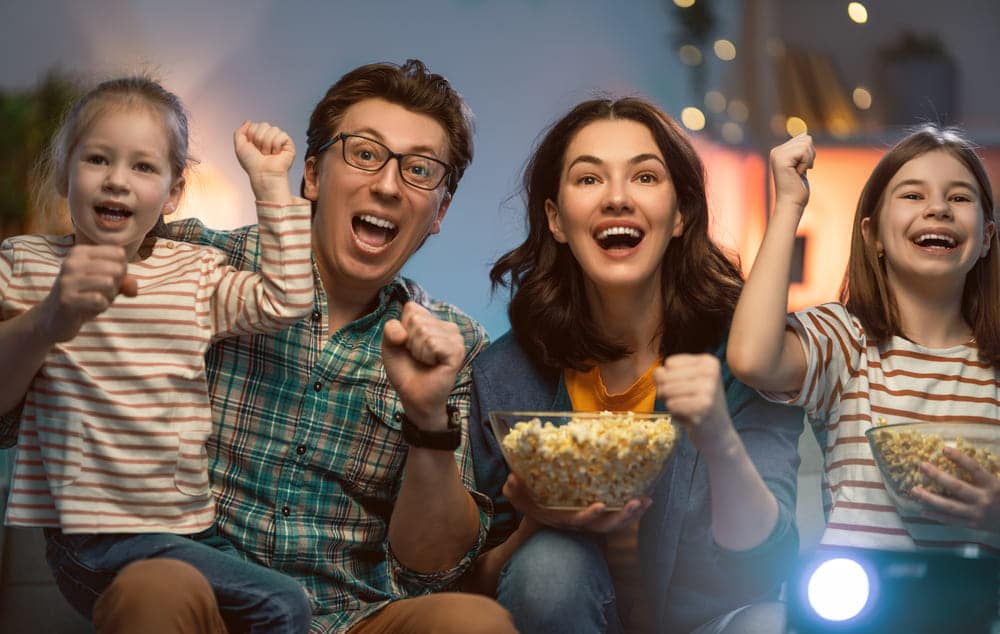 family of four enjoying watching movie with pop corn in hand.
