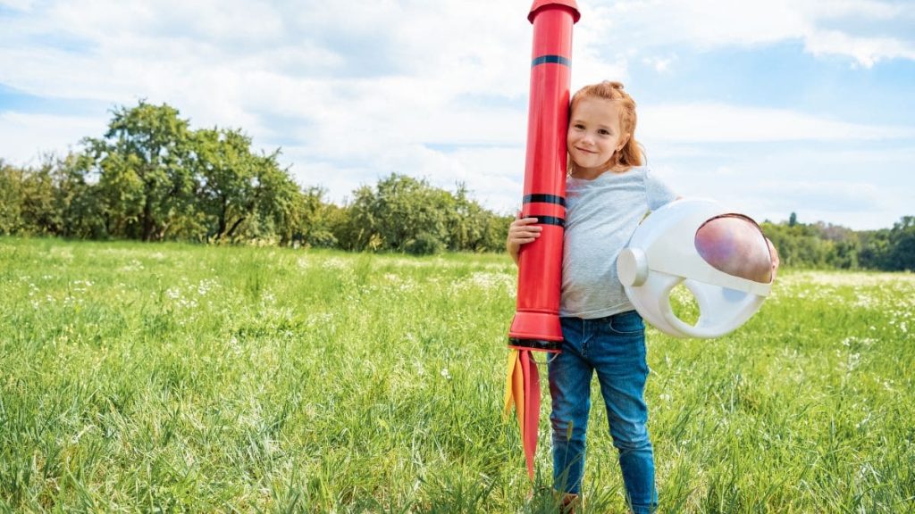 a girl outdoors holding a toy rocket.