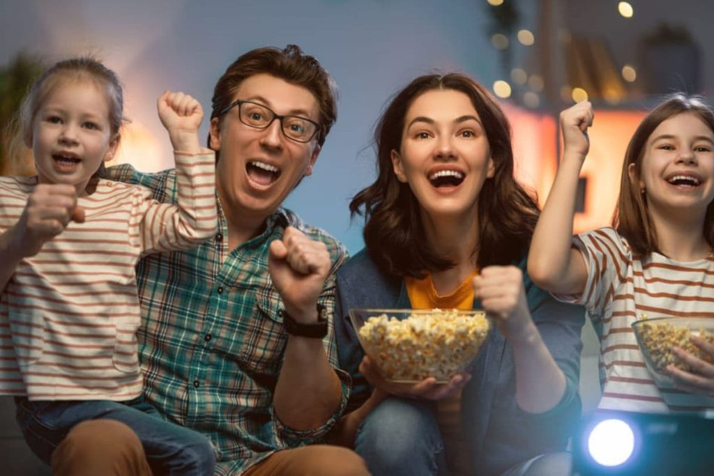 family of four enjoying watching movie on tv with pop corn in hand.