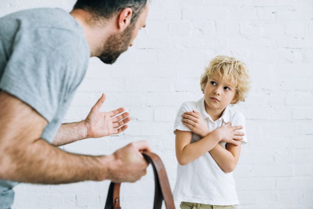 boy protecting himself looking at his father that is holding a belt.