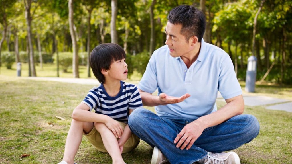 father talking to his son on a grass.