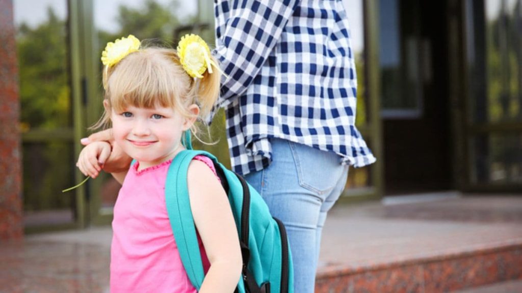 parent holding kids hands with backpack for school.