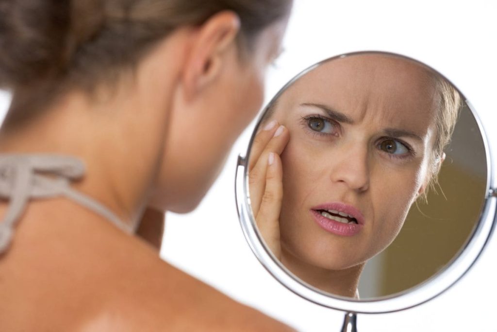 woman looking at reflection and caressing wrinkles.