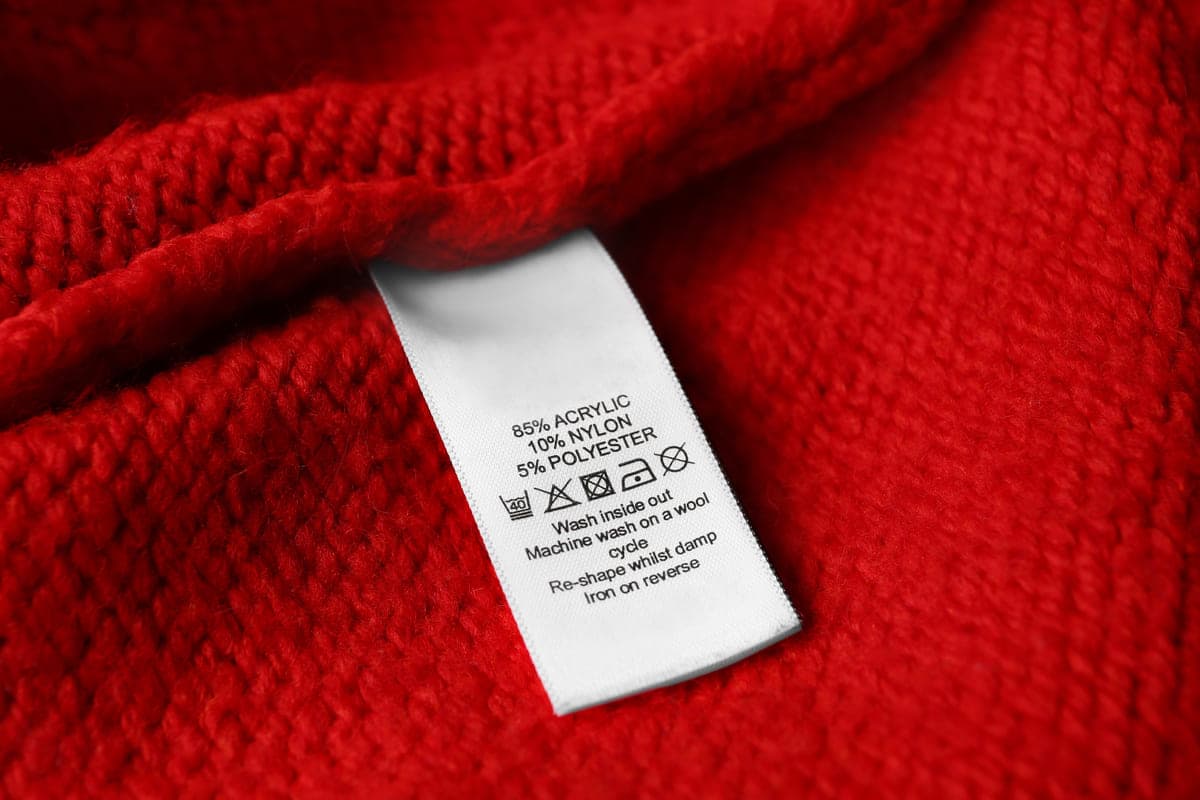 Clothing label with care symbols and material content on red sweater.