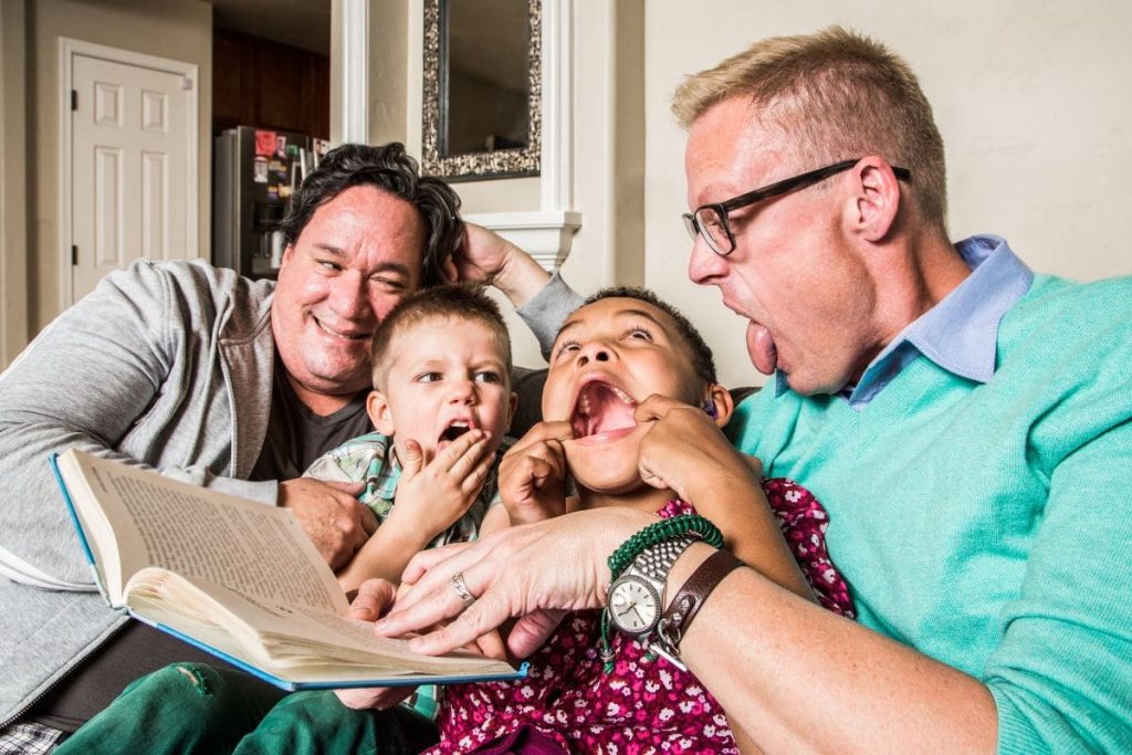 Homosexual parents reading and making faces with son and daughter.