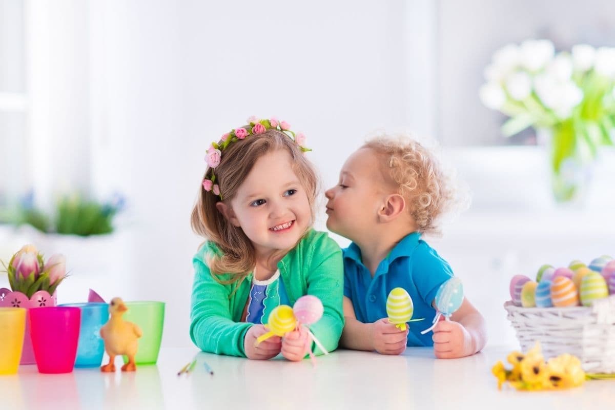 Kids painting colorful eggs. Children paint and decorate Easter egg. Toddler kid and preschooler child play indoors in spring. Decorated home with spring tulip flowers.