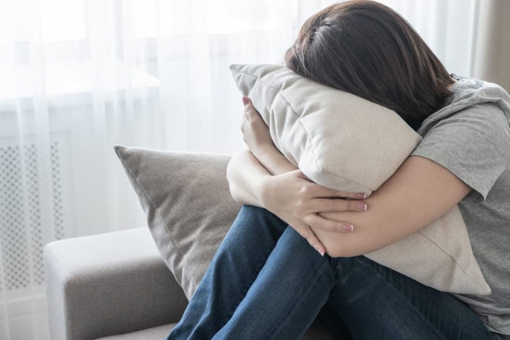 Sad depressed woman at home sitting on couch and hugging a pillow.