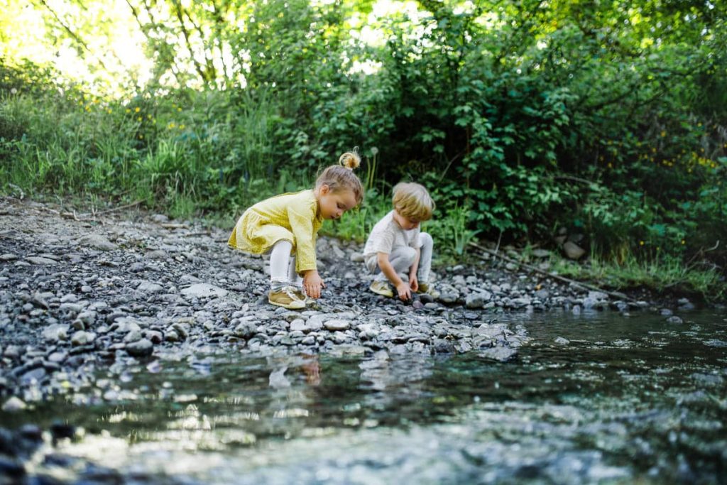 Small boy and girl playing with rocks by stream in nature.