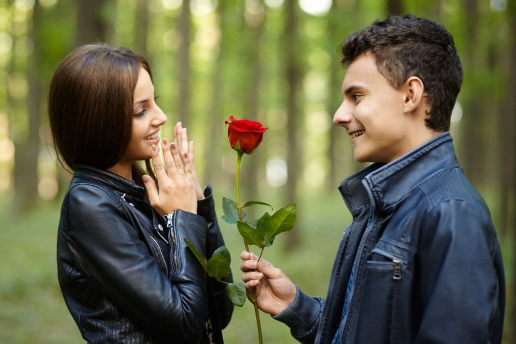 Teenage romance, a boy giving a flower to his girlfriend, outdoor in the park.