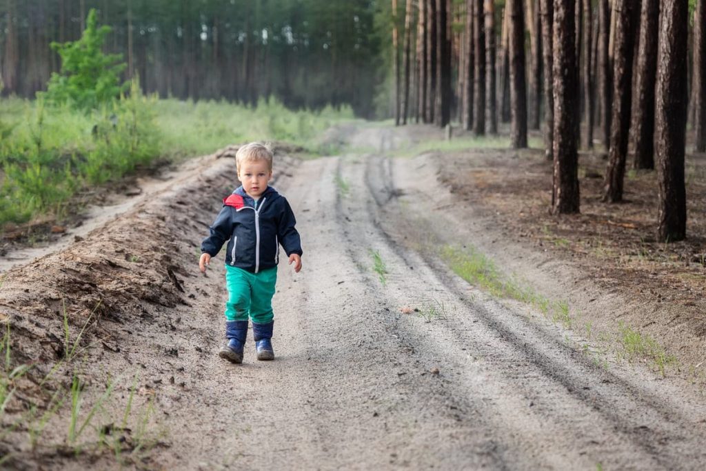 Young boy walking alone on a dirt road.