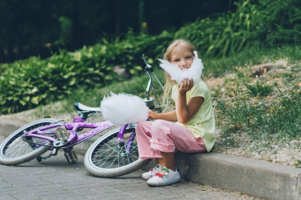 a kid girl with cotton candy on hand with a bike beside her.