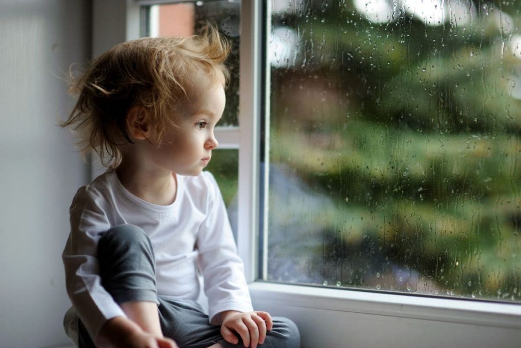 Adorable toddler girl looking at raindrops on the window.