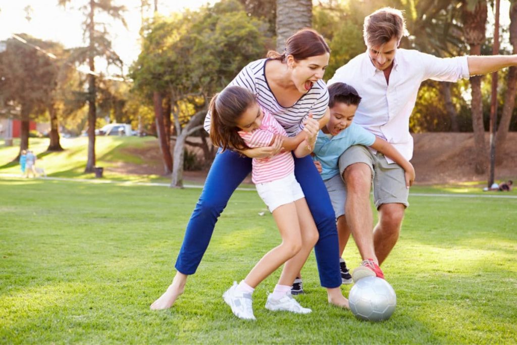 Family Playing Soccer In Park Together.