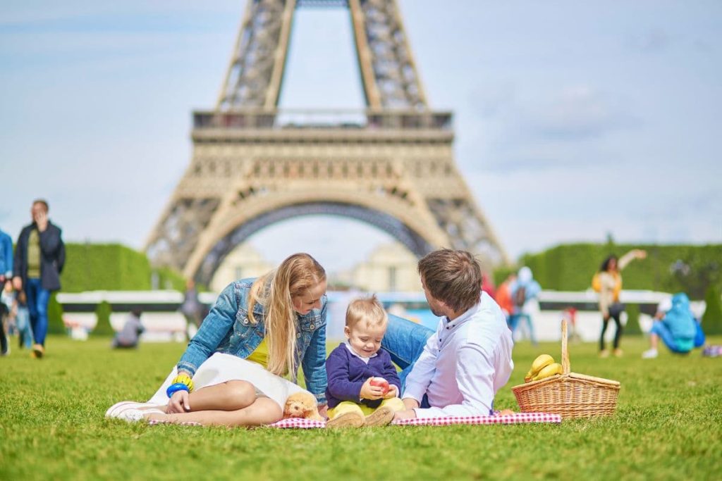 Happy family of three, mother, father and little toddler boy, having picnic in Paris near the Eiffel tower.