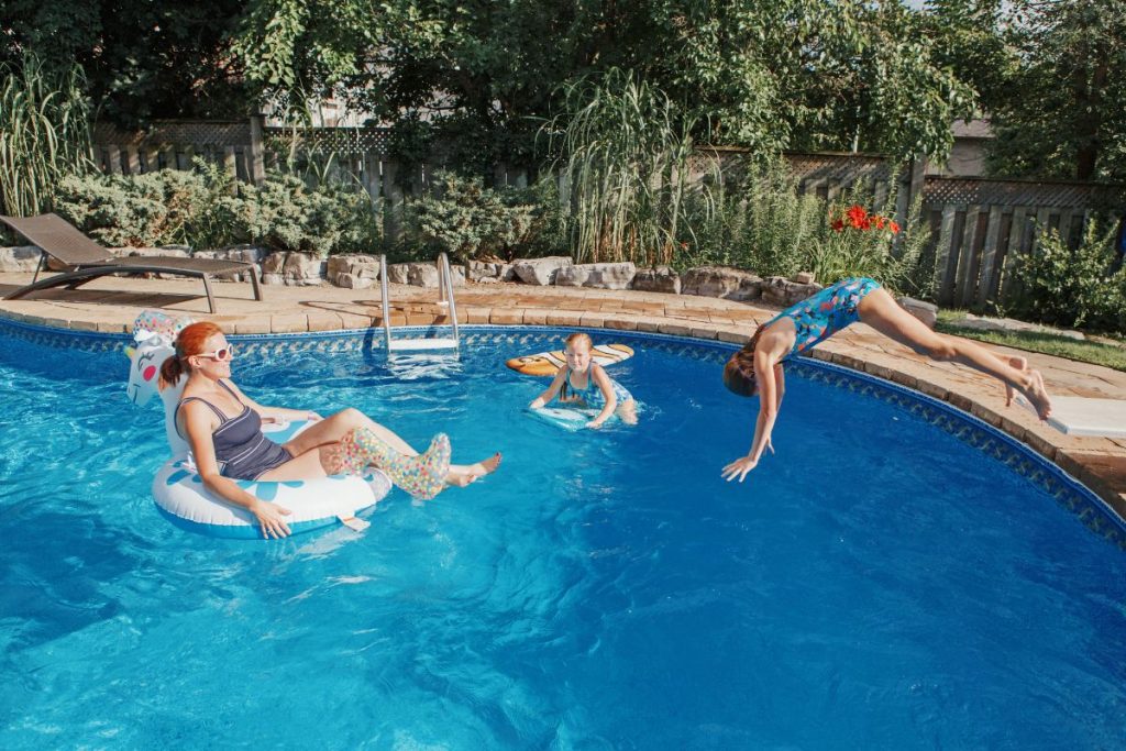 Mother with daughters children relaxing in swimming pool on home backyard. Sisters siblings diving and having fun in swimming pool together. Summer outdoor water activity for family and kids.
