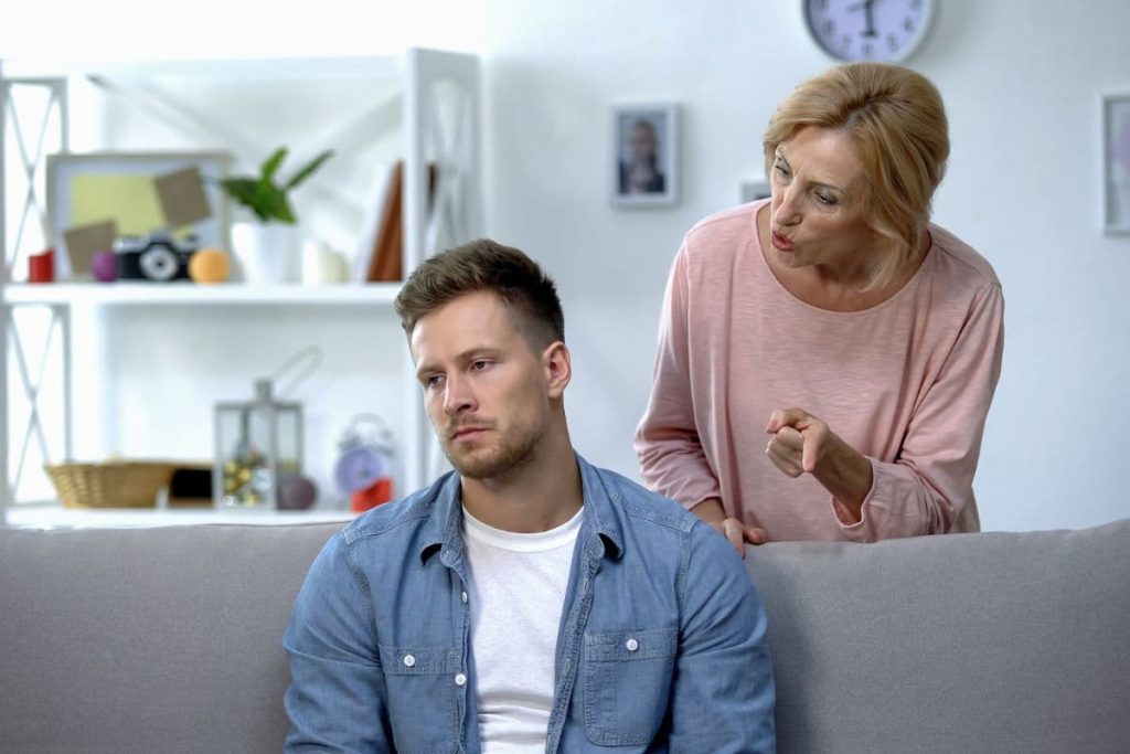 Nervous mother talking to adult son sitting on sofa at home, family conflict.
