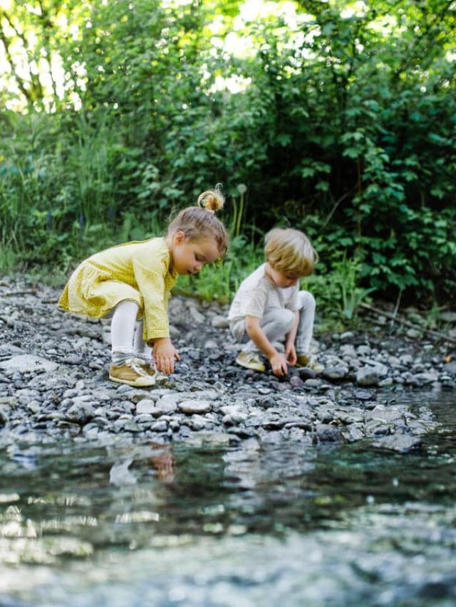 Small boy and girl playing with rocks by stream in nature.