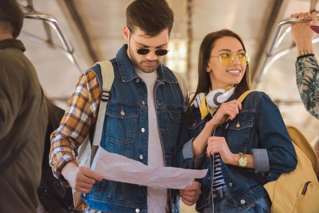 female and male traveller with headphones and glasses on a train the male holding the map.