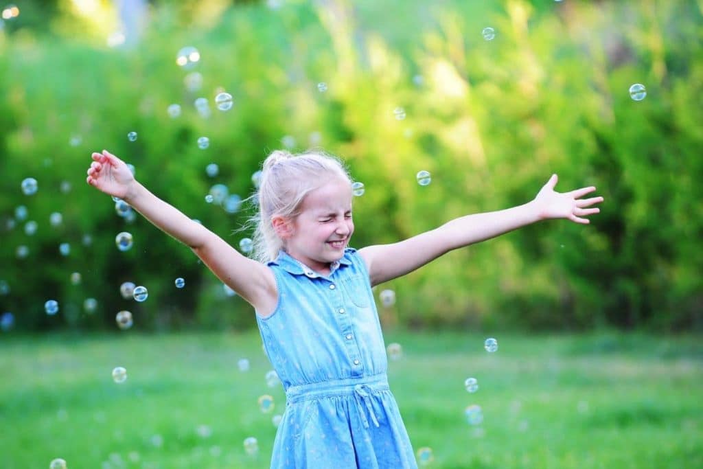 girl play with bubble blower on green lawn.