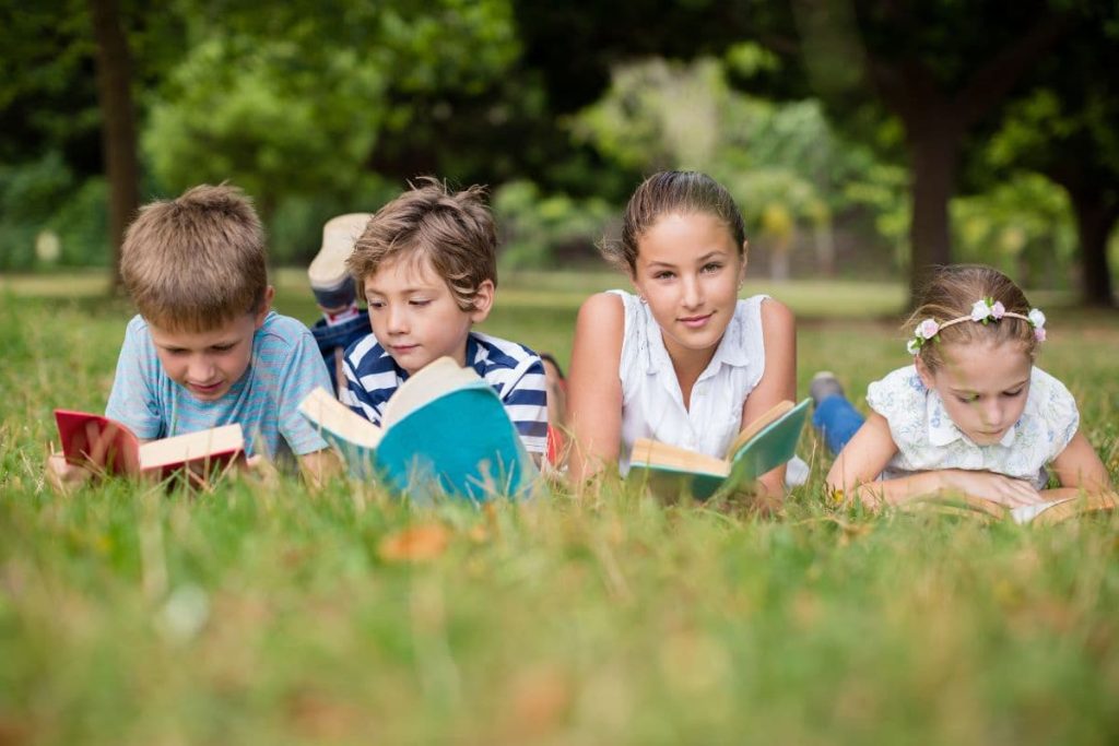 Kids lying on grass and reading books in park.
