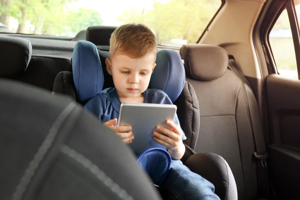 Little boy with tablet computer buckled in car seat.