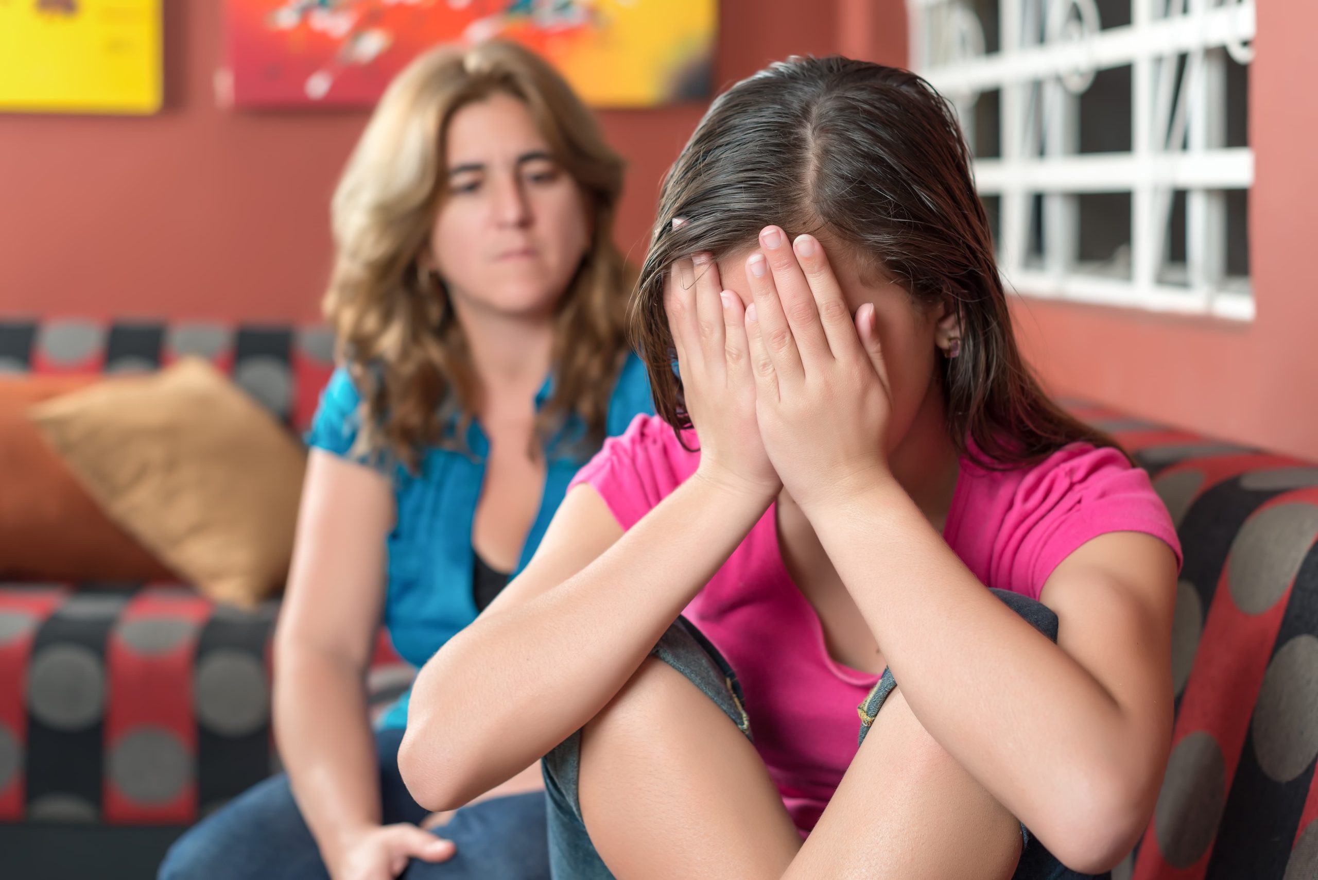 Sad teenage girl cries next to her worried mother.