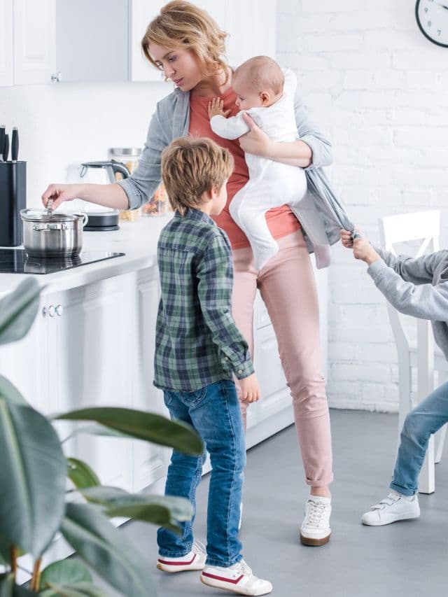 Tire mother cooking while holding infant and naughty kid pulling.