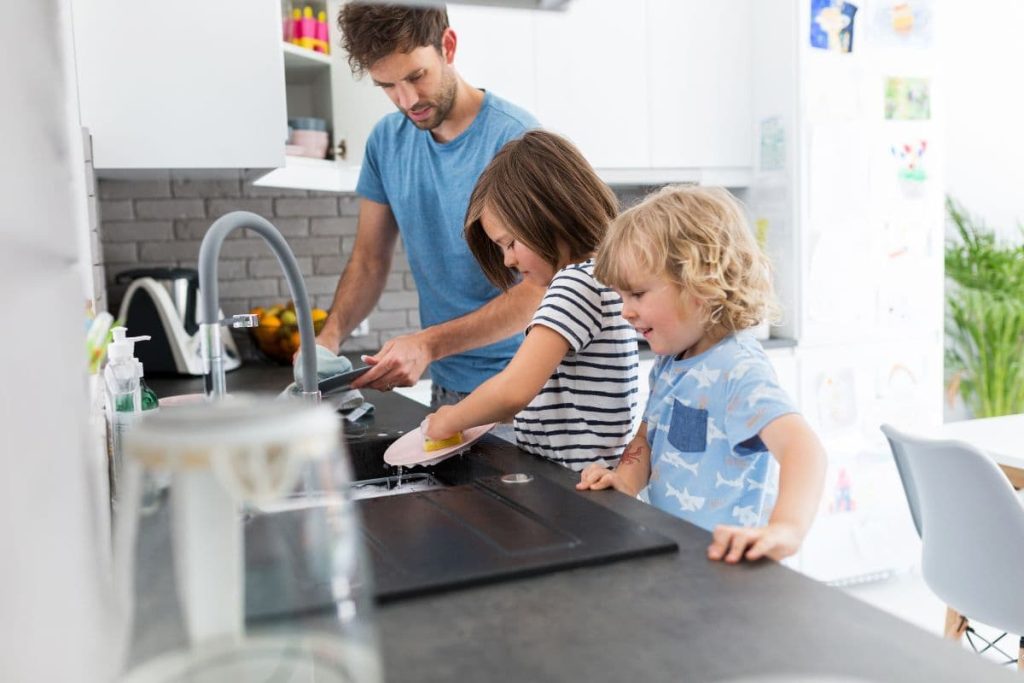 children helping their father doing chores by washing the dishes in the kitchen at home.