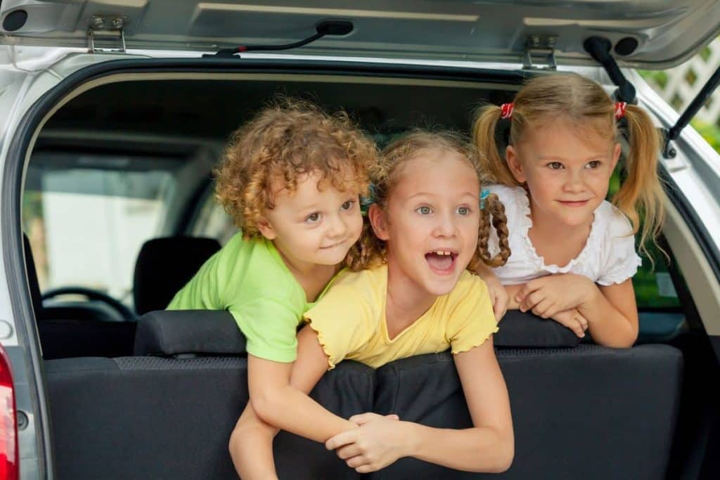 three happy kids in the car looking outside.
