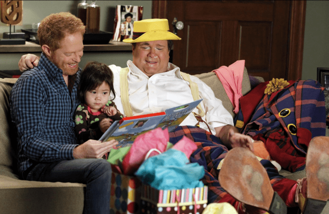 two father with their adopted daughter in the middle sitting in a sofa.