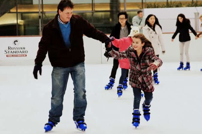 father and daughter ice skating indoors.